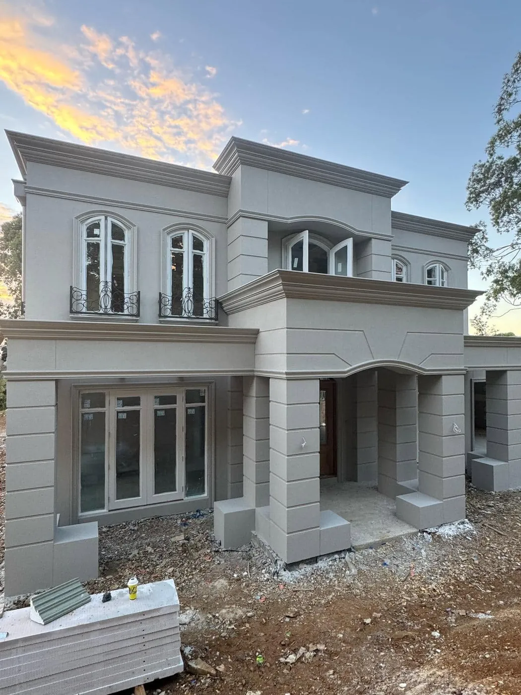 French provincial home with arched windows, Juliet balconies and a columned portico, rendered in light grey