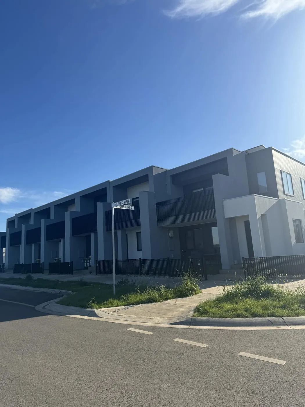 Row of new rendered townhouses on a corner street under blue sky